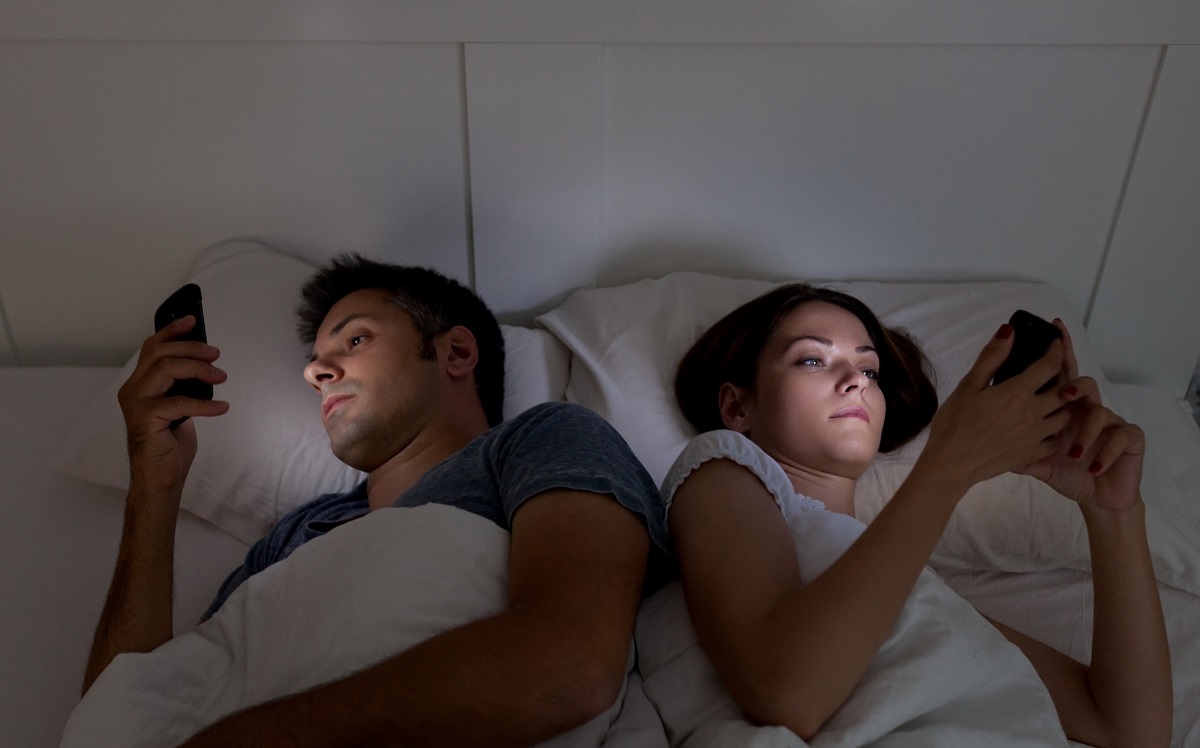 photo; a couple looking at their smartphones in bed