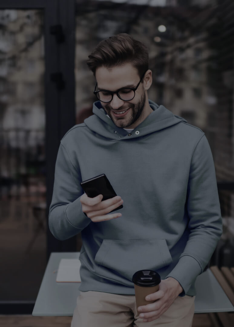 Young professional holding a coffee and smiling while browsing his phone