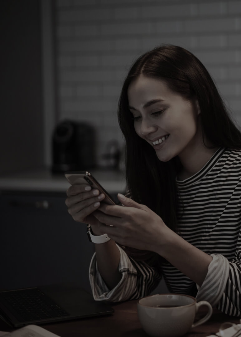 Young lady sitting at her kitchen while smiling at her phone